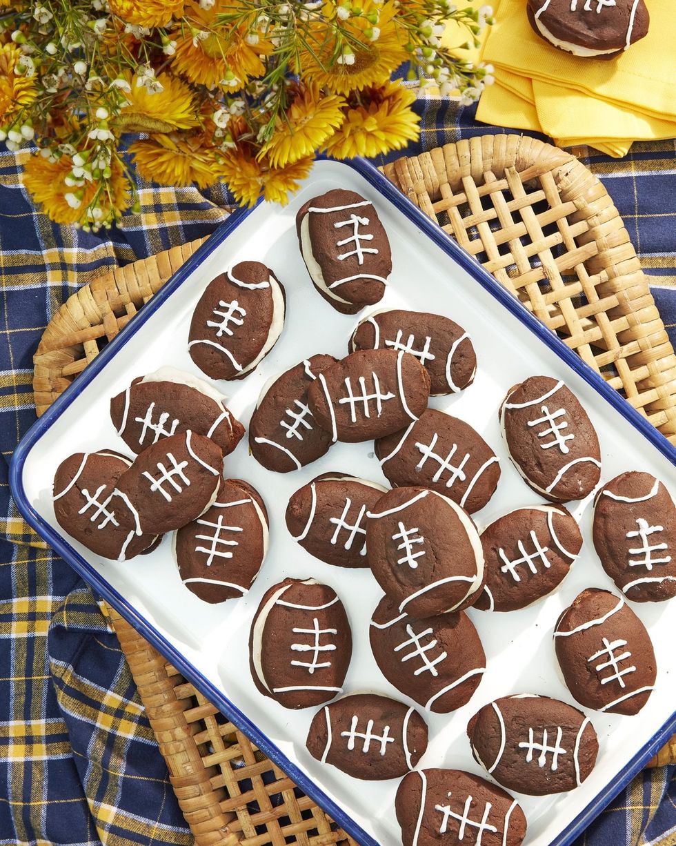 chocolate whoopie pies with cinnamon cream filling decorated on top to look like footballs and arranged on a white serving tray with blue trim