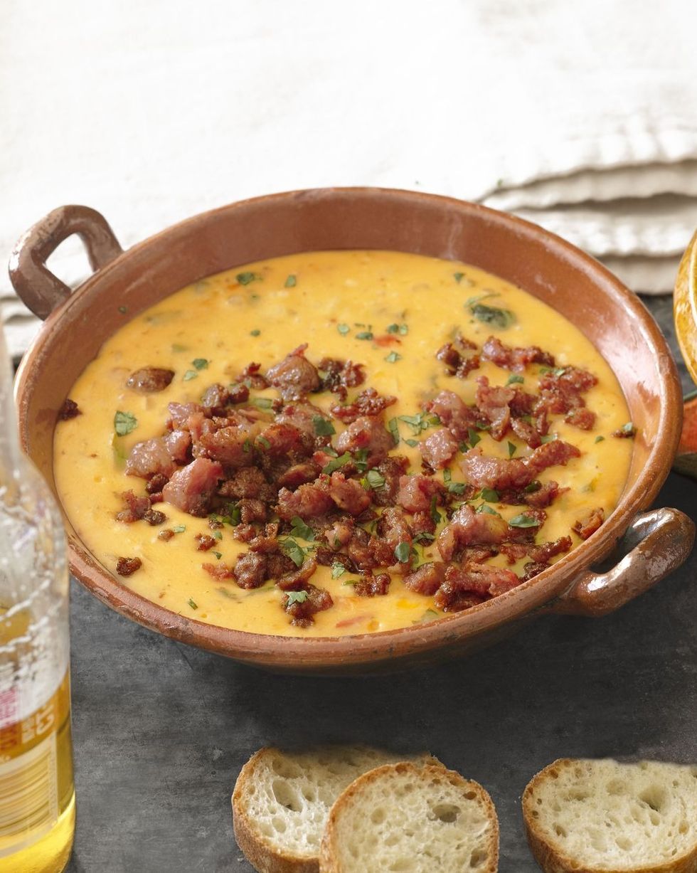 queso fundido in a light brown bowl with roasted poblano peppers and chorizo on top and sprinkled with chopped cilantro