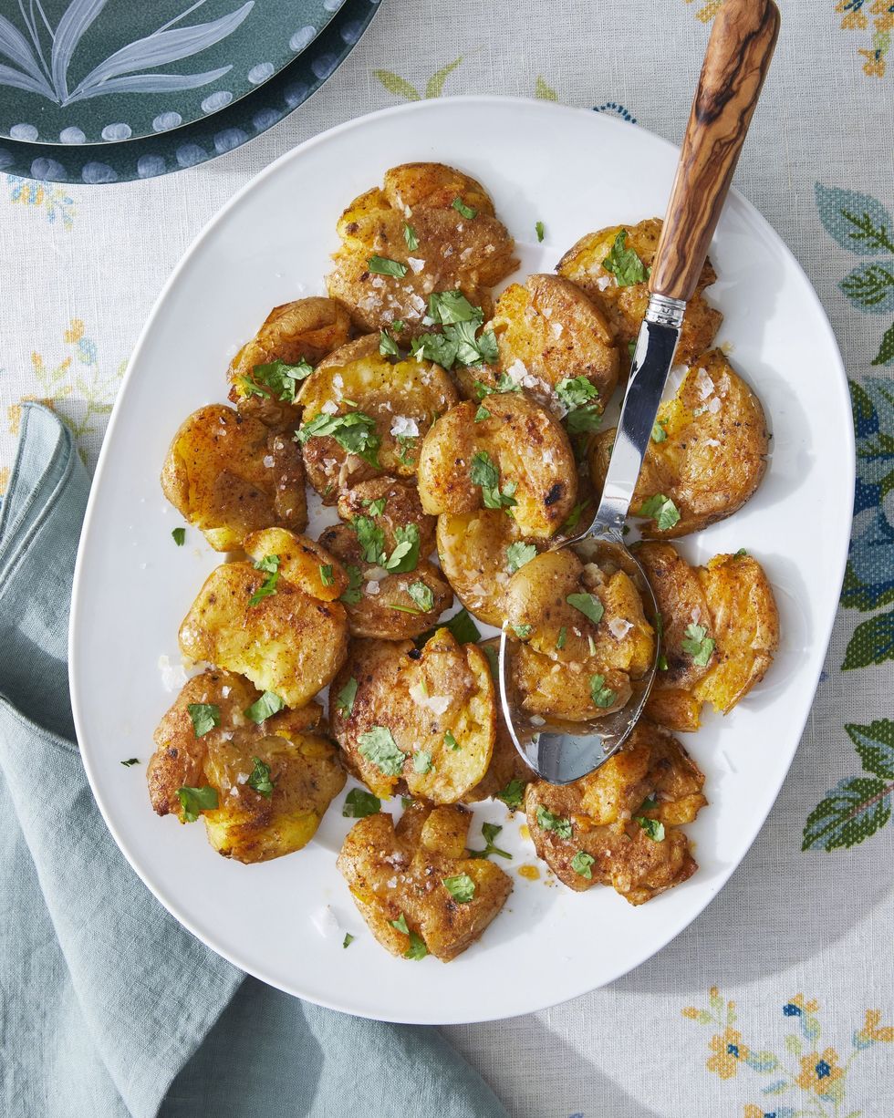 smashed potatoes with paprika and cumin on an oval white plate with a spoon for serving